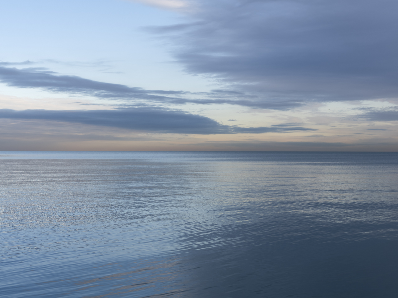 a beautiful morning on the lake from the Lake Series, January 2020, where the lake waters create a mirror, reflecting the dramatic clouds in the light blue sky with a warm tinged horizon of yellows and peaches