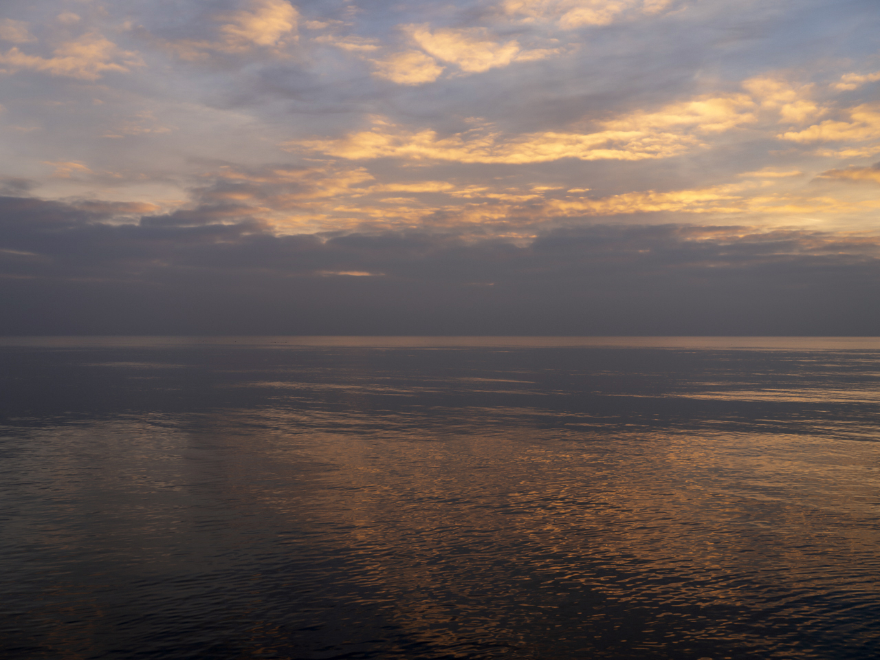 a Painterly Lake Photo where the sun reflects off the bottoms of the purple clouds that lightly fill the sky as the lake shows a mirror image beneath in the still waters