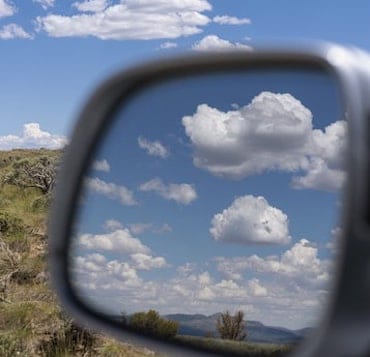 perfect clouds sit in a light blue sky in arid Utah, reflected in the rearview mirror of a car