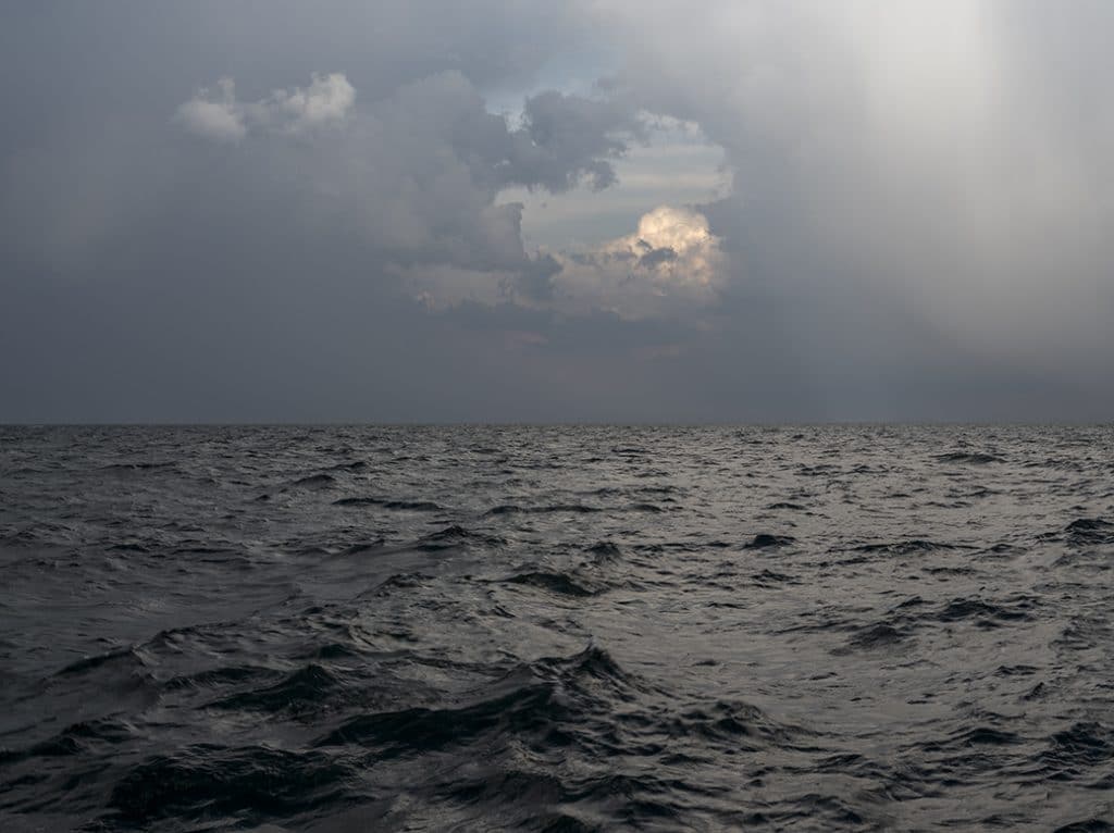 Illuminated clouds appear in a space between heavier storms on Lake Michigan. The waters are stirring as rains begin to fall.