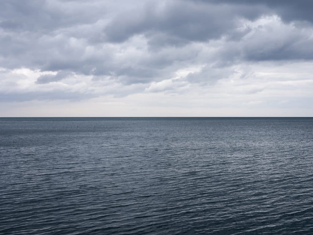 A mid-April morning on the lake featuring dark slate gray waters rippling in the wind. Clouds are illuminated in the sky above.