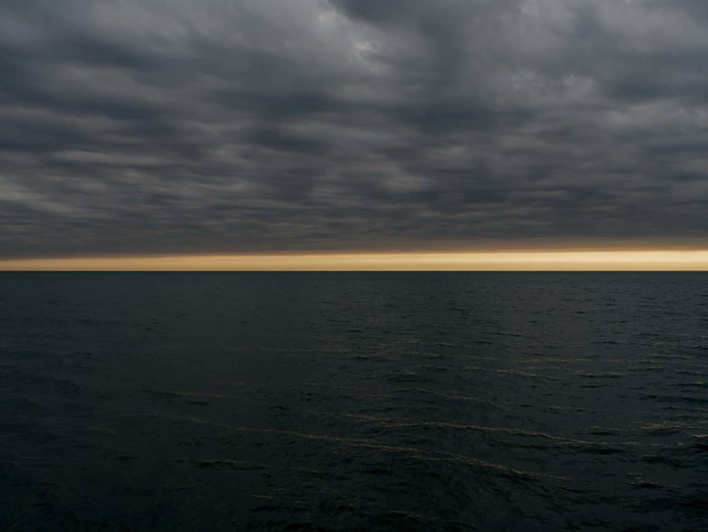 A moody lake morning greets me as I arrive to Lake Michigan. A golden band sits just above the horizon line. The clouds illuminated from behind by the rising sun.