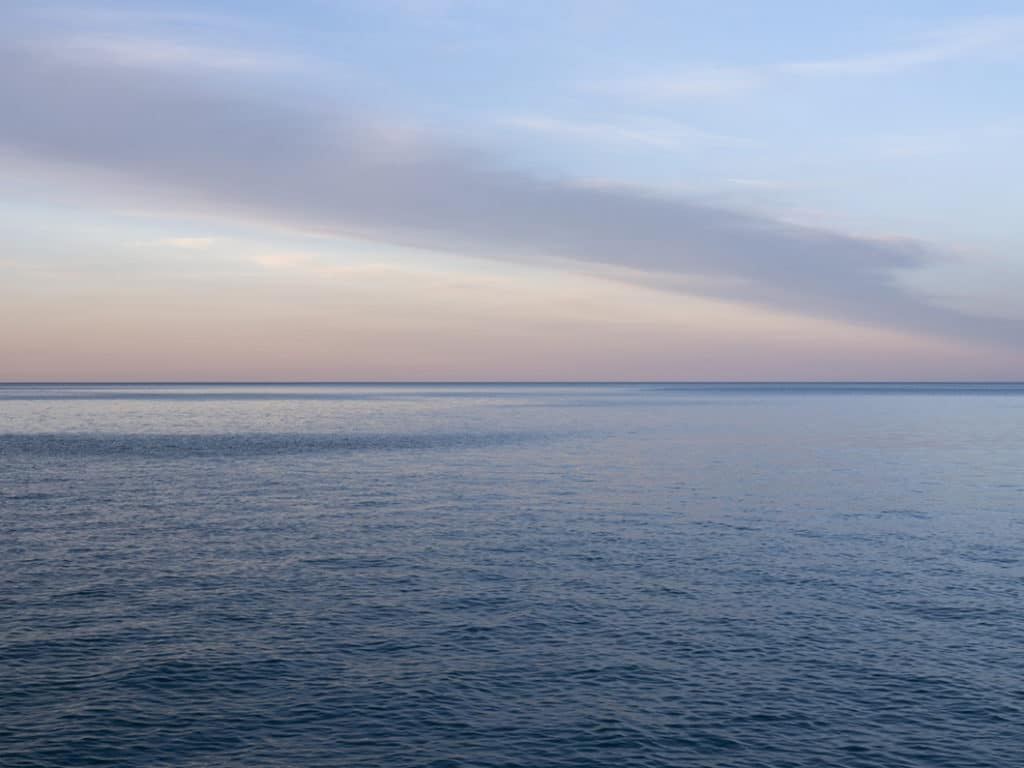 an artwork by Lincoln Schatz called Lake Michigan: Closer to the Sun (1) featuring a lake landscape from early in the morning with soft pastel light over rippling lake waters