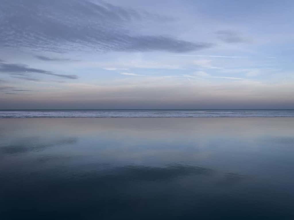 A serene lake photo from a morning on Lake Michigan where the sky is reflected in the still waters that stretch to the horizon line. From the Lake Series, winter of 2022.