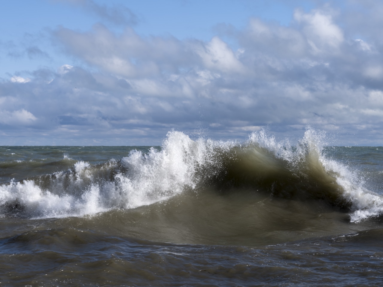 The waves are crashing on Lake Michigan in this photograph from September 28th, 2022. With winds and storms building, the lake waters churn and push towards shore in a powerful repeating rhythm. Tossing rocks and logs easily onto the lake wall by the time this storm is through.