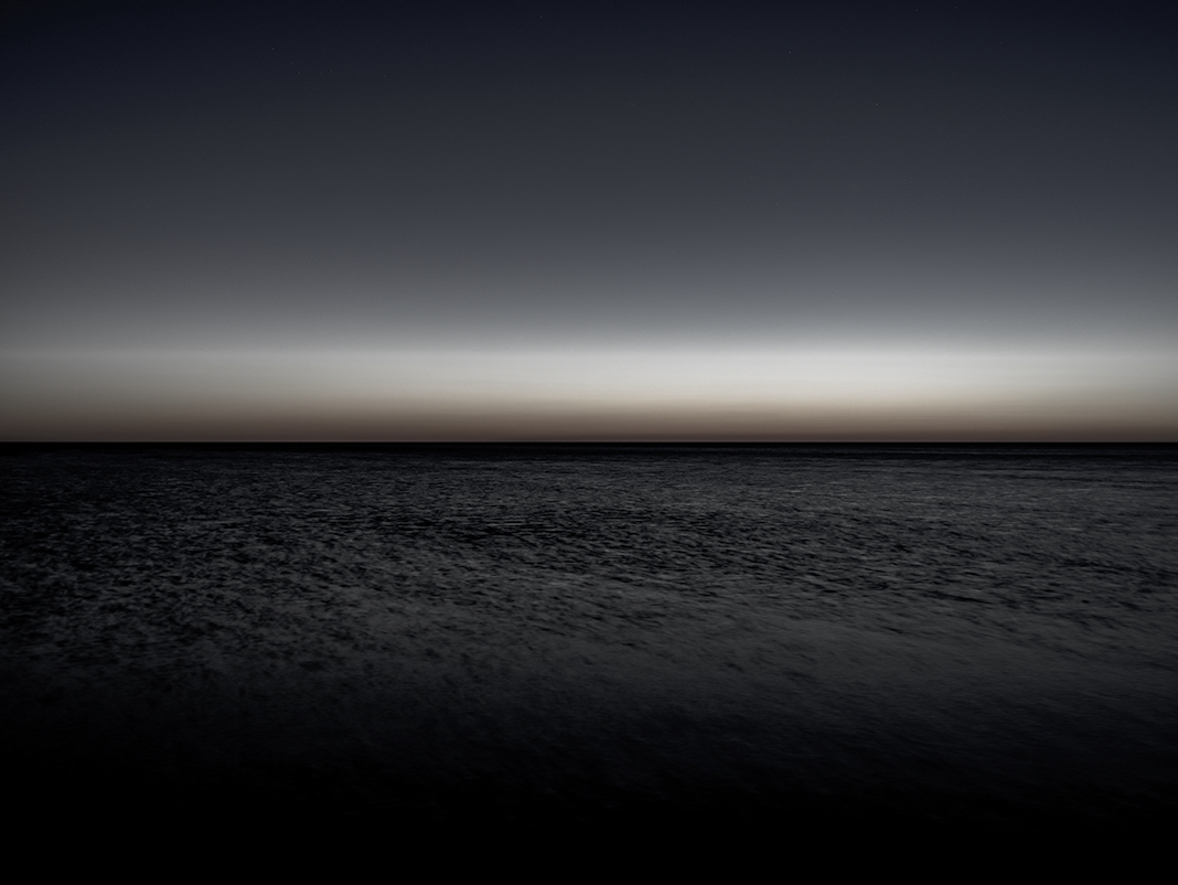 A black and white lake dawn. First light on the lake and the sun is just barely beginning to illuminate the water. Waves shift in the light, restlessly moving in this photograph from the Lake Series.