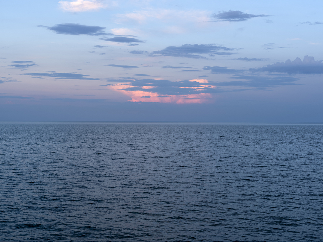 The clouds layer in the sky, oscillating between cool and warm as dawn arrives to Lake Michigan at the end of May 2020. The winds that are present seem to only bother the water. The clouds hang in the sky, unmoving as they shift into color, contrasting with one another and the clear blue sky above.