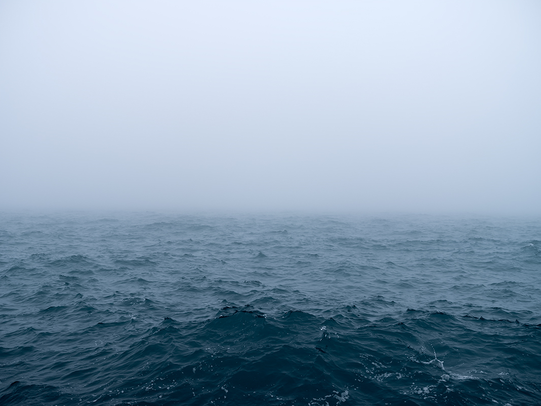 The larger landscape has completely vanished, the horizon of the lake has disappeared. The waters are choppy, moving quickly and crashing into the wall I stand on. Storms will arrive. But for now, everything is covered in fog. Giving the feeling, although an illusion, that I am alone with the lake.