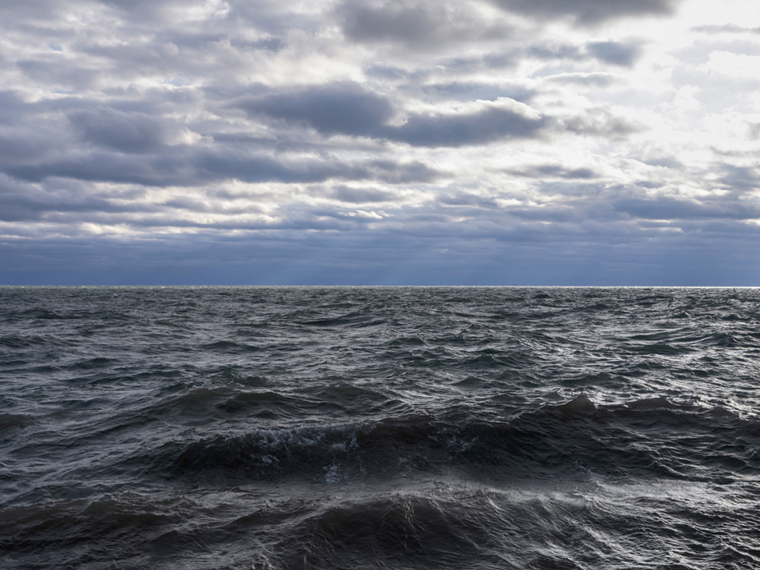 Lake Michigan pushes against the wall underneath where I am standing. The sun pushes through clouds out over the water and the light is illuminating the lake in a thin line near the horizon.