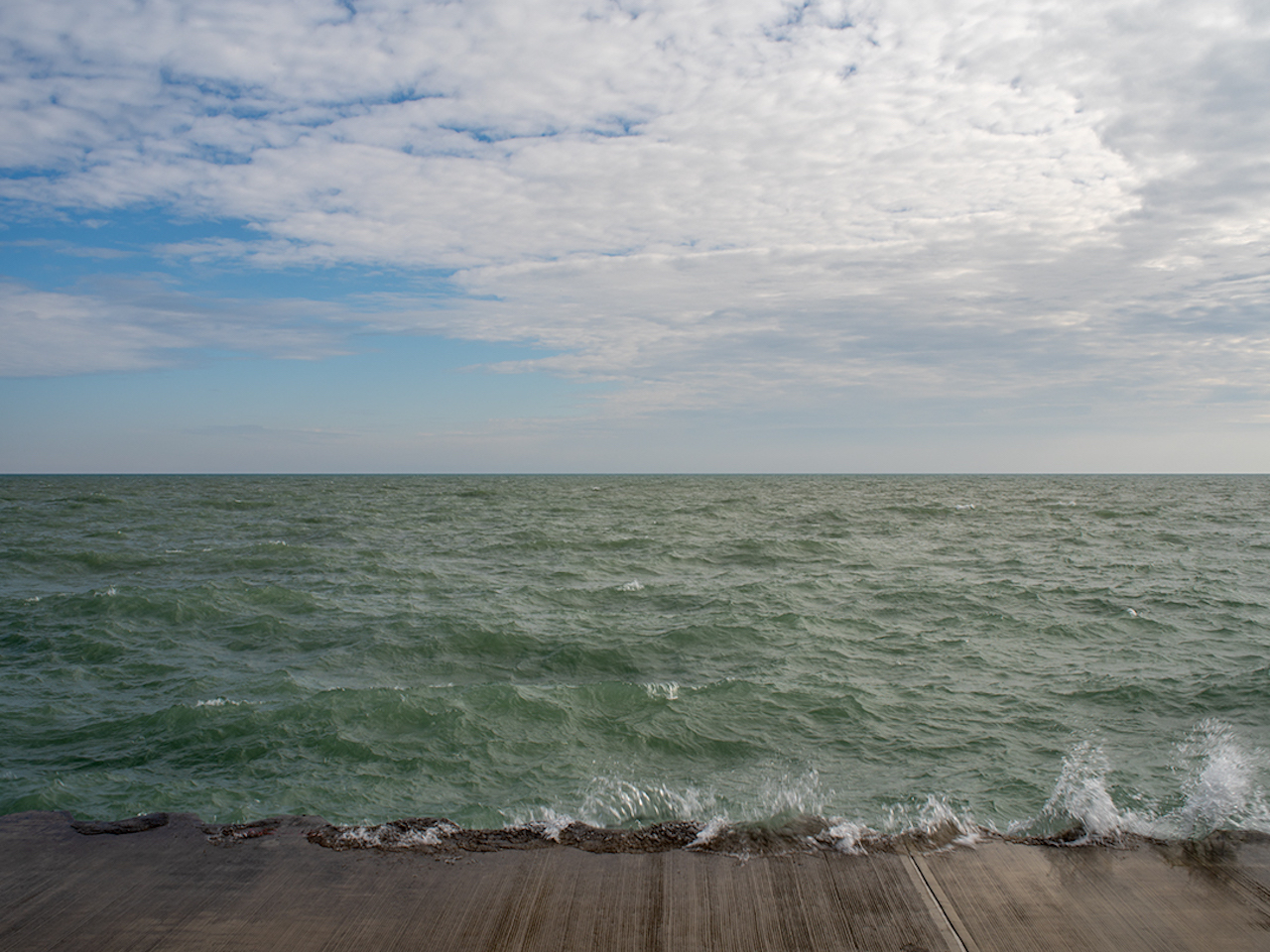 Water strikes the concrete wall north of downtown Chicago. A serrated wall appears and disappears again and again along the city's eastern edge. Forcing an abrupt stop to the rocking lake water.