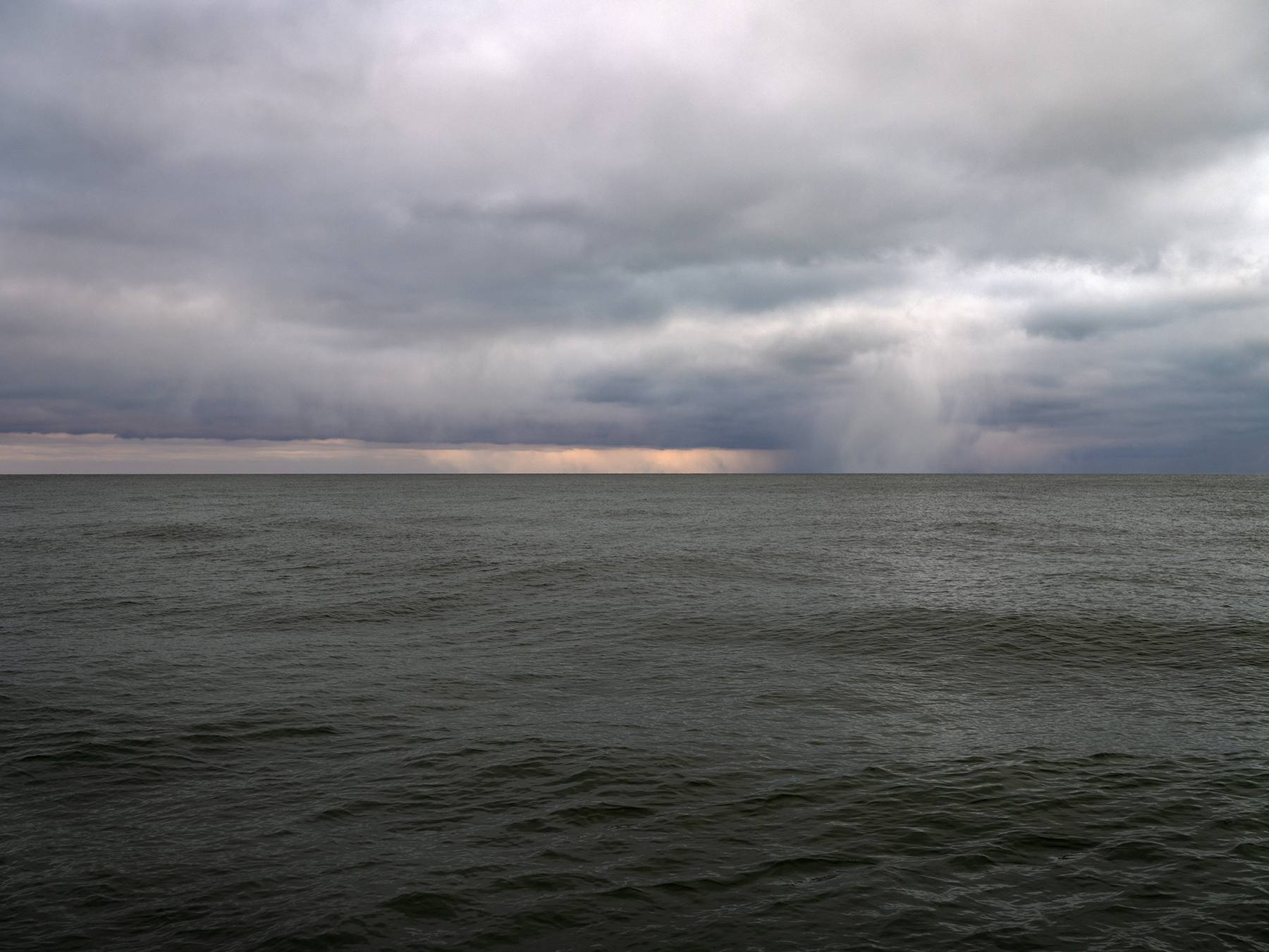 DSCF2558 Storm clouds are rapidly changing form in the skies over a green gray Lake Michigan in a photo from the Lake Series by Lincoln Schatz.
