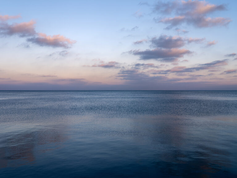 A soft blue morning with pastel colored clouds in the sky over a lightly rippling Lake Michigan in a photo from the Lake Series by Lincoln Schatz.