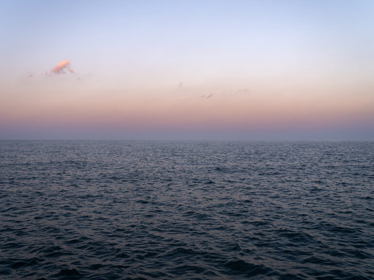 A pastel morning on the lake with a few light clouds in the sky as it shifts from purples to blues in a photo from the Lake Series by Lincoln Schatz.