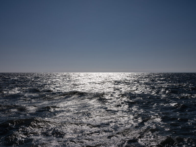Sunlight reflects brilliantly off the surface of a dark blue black Lake Michigan while clear blue skies sit overhead in this photo from the Lake Series by Lincoln Schatz.