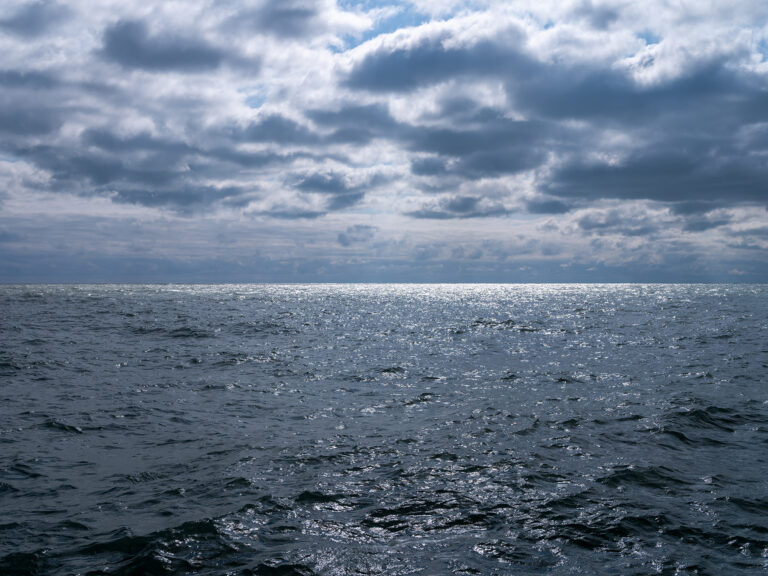 The sun is dazzling as it cuts through dark clouds and strikes the surface of a rippled Lake Michigan.