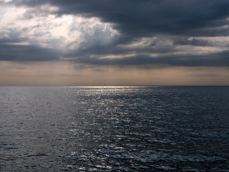 A dark and storm filled morning on the lake turns sky and water deep maroon and gray alongside flashes of bronze near the horizon.
