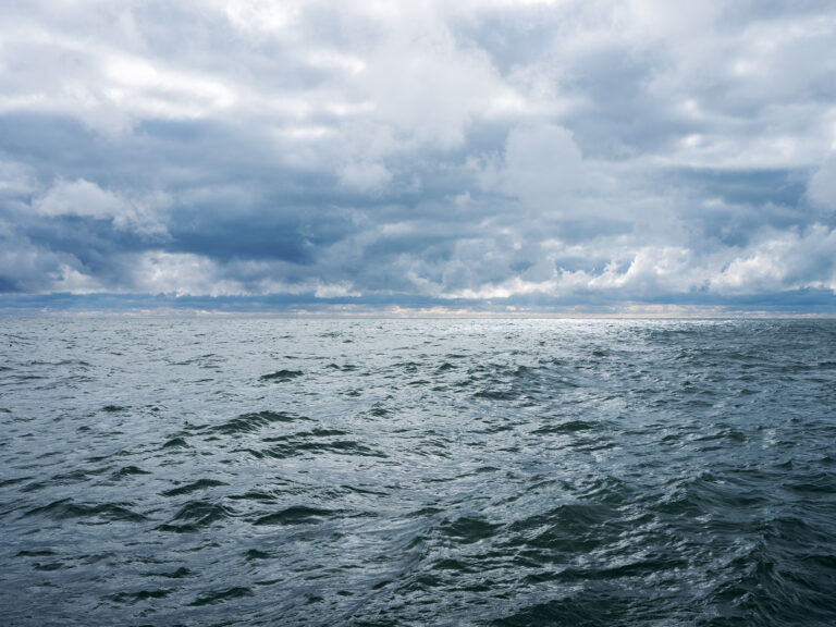 A somewhat surreal stormy day on Lake Michigan where clouds are piling up in a disarray in the sky over a choppy green blue Lake Michigan in a photo from the Lake Series by Lincoln Schatz.