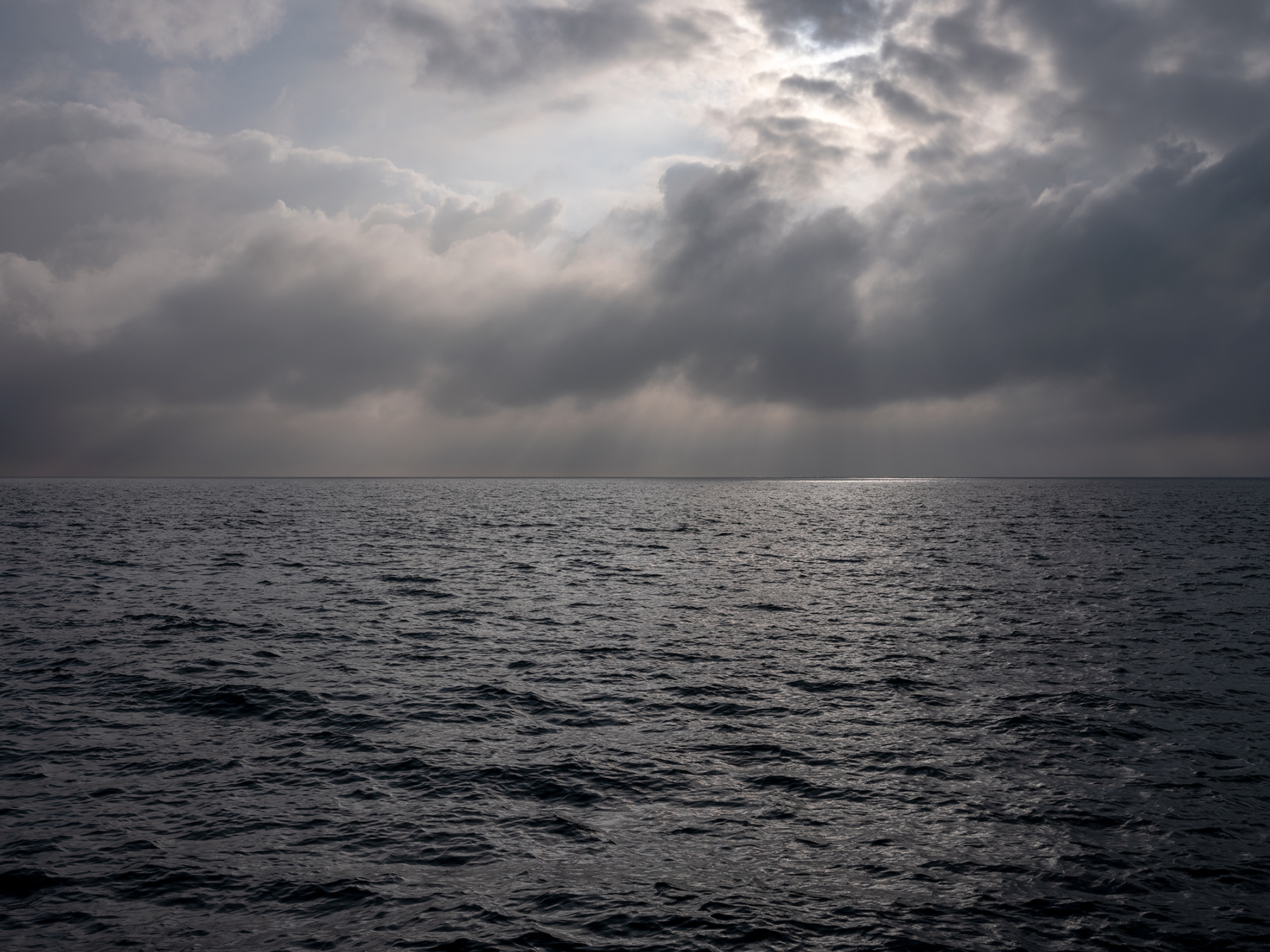 DSCF8552 Gray and dark clouds break apart to allow ethereal light to pass through over an almost black Lake Michigan in a photograph from the Lake Series.