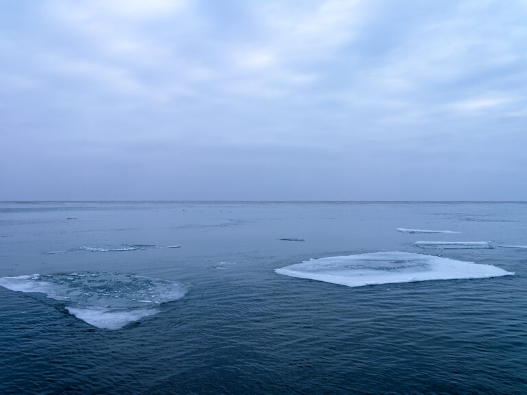 Large pieces of ice float in a freezing cold Lake Michigan under a cloudy blue gray sky.