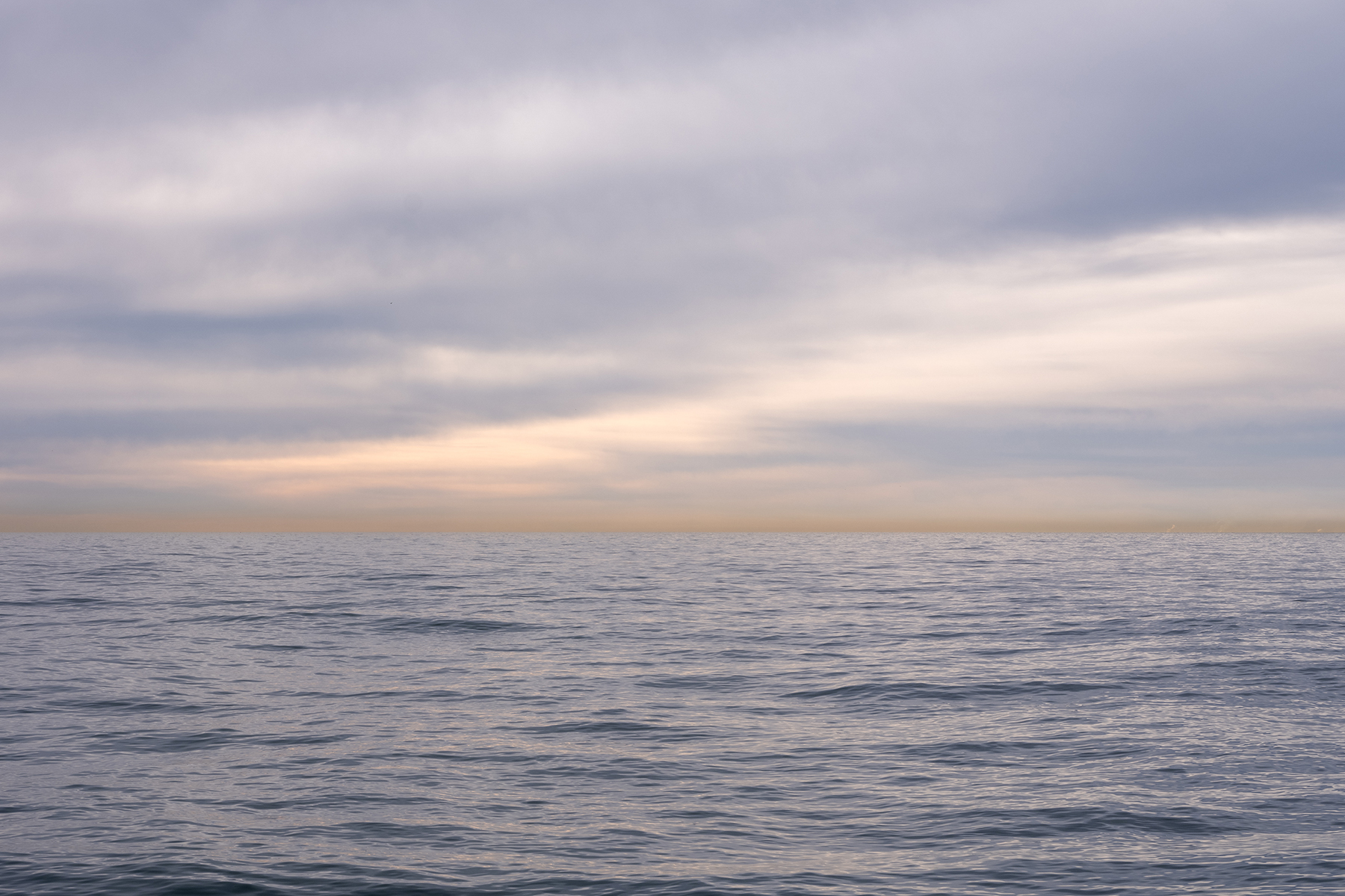 A detail image of soft purple clouds over a lake that mirrors the gentle pastels of the sky overhead in this photo from Lake Vistas by Lincoln Schatz.