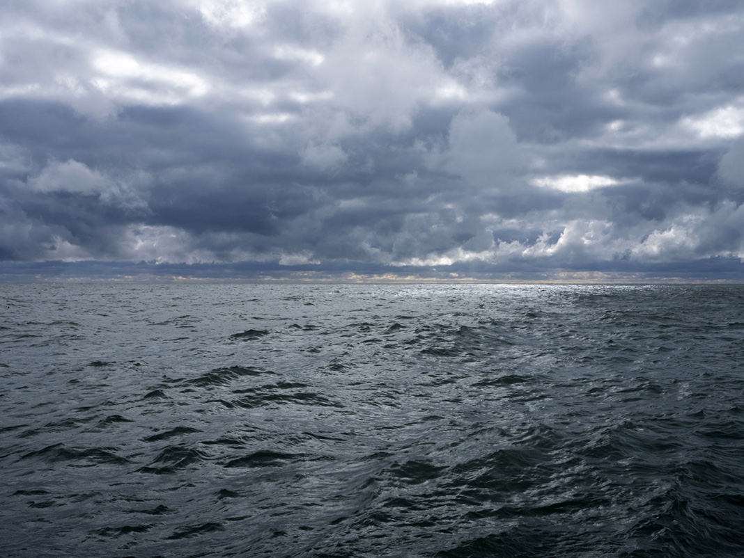 Storms push through on August 30th, 2023, but for a brief moment a circle of brilliant white light appears out on the lake far away from shore as I photograph. This light causes the water to flash and shimmer while the rest of the landscape moves into deeper and more dramatic tones.