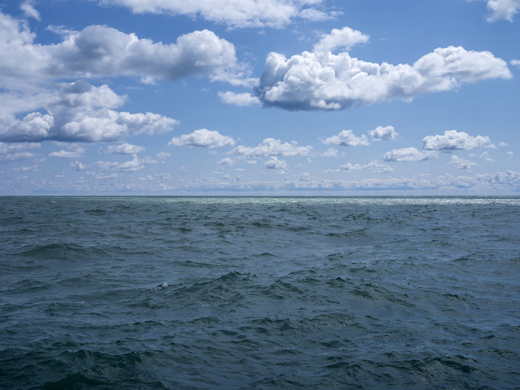 Clouds are perched in blue skies, separated from one another, creating a rhythmic pattern over a blue-green Lake Michigan from July 18th, 2024.