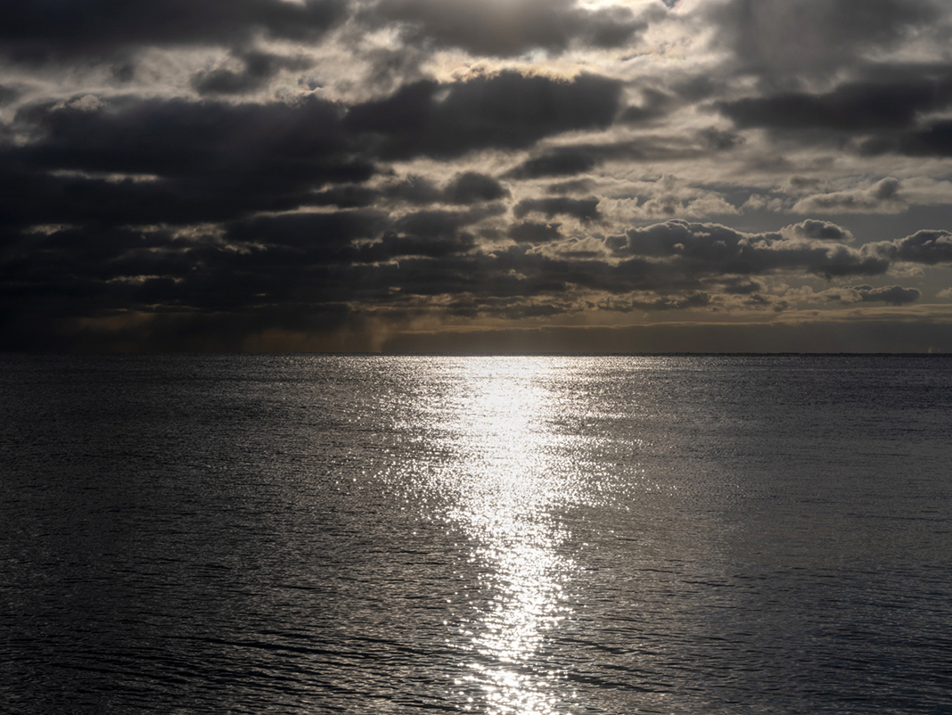 The sun shimmers in a path on Lake Michigan while heavy clouds sit in the sky overhead. Storms will arrive soon. It is late November 2023 and the path of the sun in the sky has changed dramatically from summertime.
