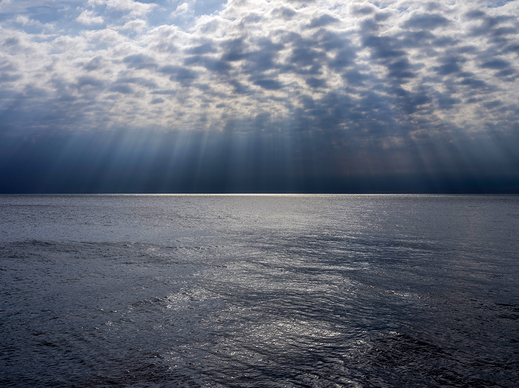 Rippling cloud formations over Lake Michigan create slashes of sunlight that illuminate the water out near the horizon. Forming a pool of brilliant light in contrast with the dark, storm filled landscape, that surrounds it.