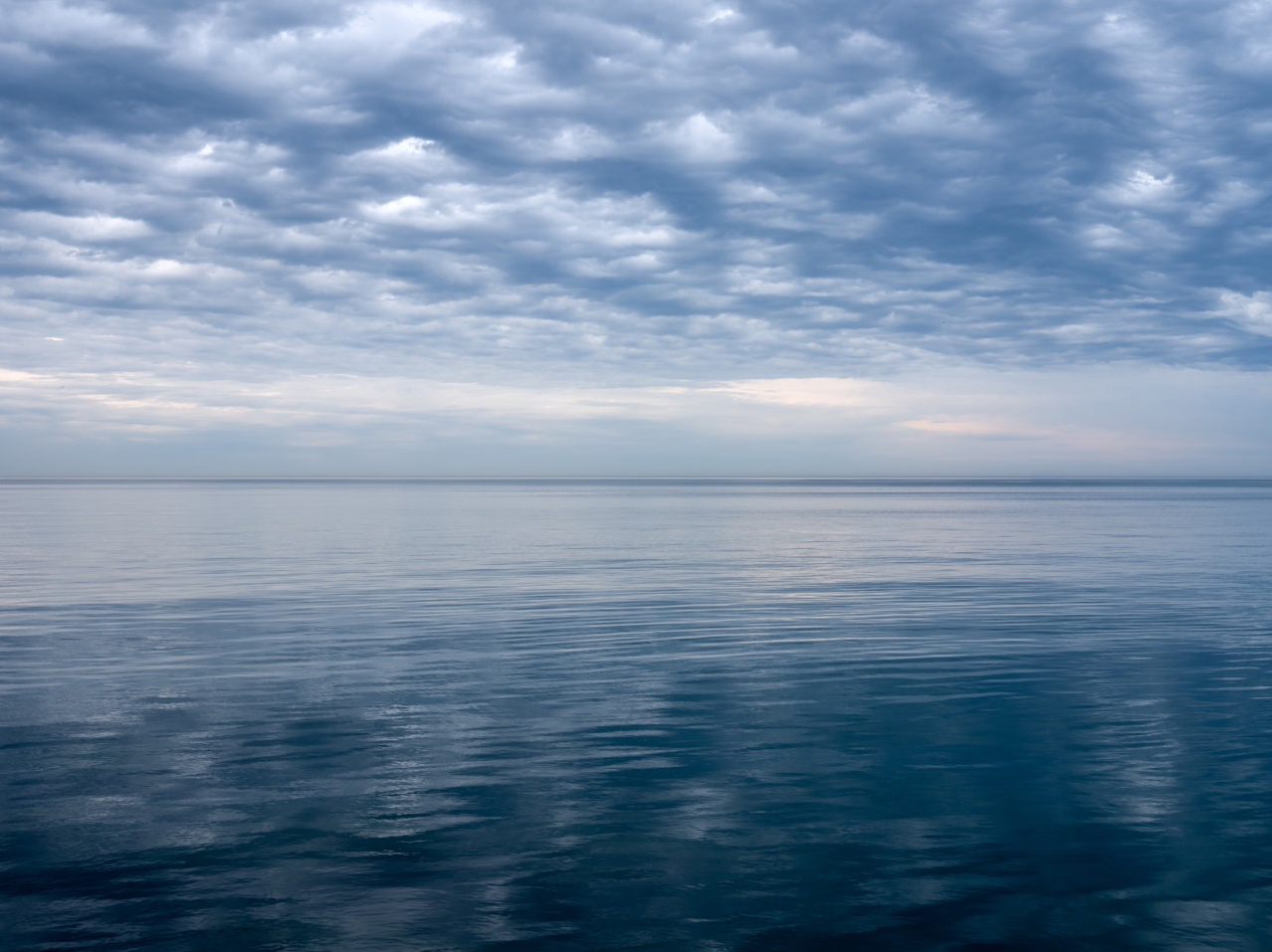 Almost still lake waters create a mirrored reflection of the dappled clouds in the sky. A photograph from the Lake Series, an edition of fine art photographs spanning nearly ten years.