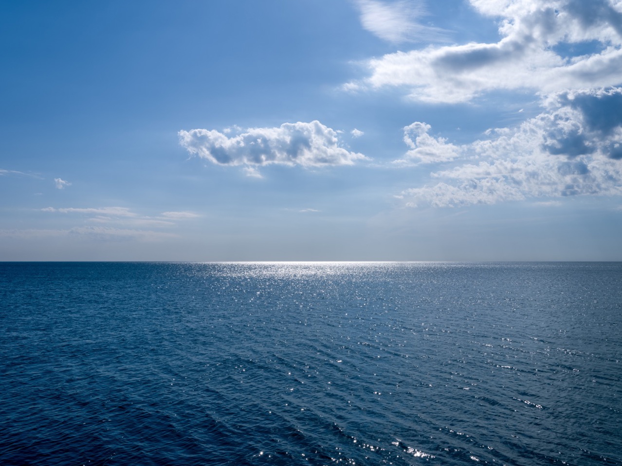 Sunlight strikes the surface of Lake Michigan, creating a dazzling brilliance of light as gauzy clouds stretch and slowly transform in the sky overhead.